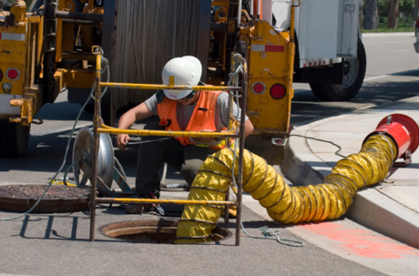 Utility worker kneeled down on street near manhole where ventilation is going in.