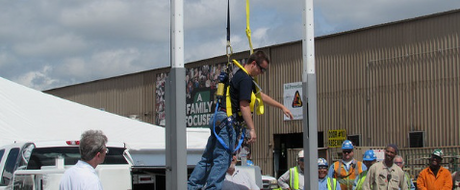 Man suspended while wearing safety harness. People gathered around him from what appears to be a safety demonstration.