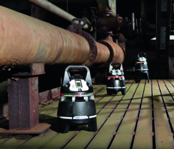 3 Draeger X-zone 5000 gas monitors in a dimly lit facility with a large metal pipe next to them.