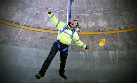 Worker wearing a harness dangles with his arms and legs spread out and hard hat falling out of his hands.