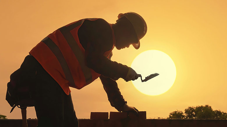 Worker laying bricks under a hot sun.