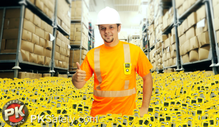 Man gives thumbs up while standing in a large pile of yellow gas monitors in a warhouse.