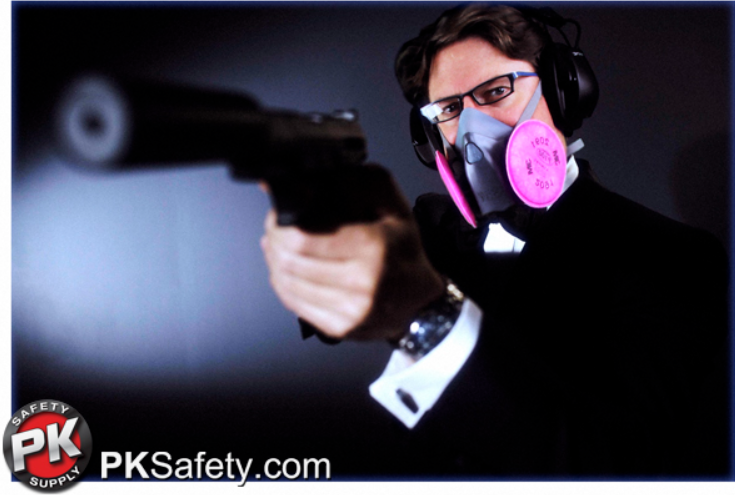 Guy dressed in suit holding gun while wearing respirator.