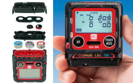 A hand holds a compact gas detector with a digital display showing readings. Next to it, disassembled components and sensor parts are laid out.