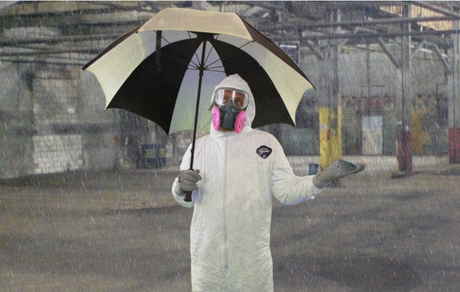 Worker wearing hazmat suit and respirator holding an umbrella inside an industrial building.