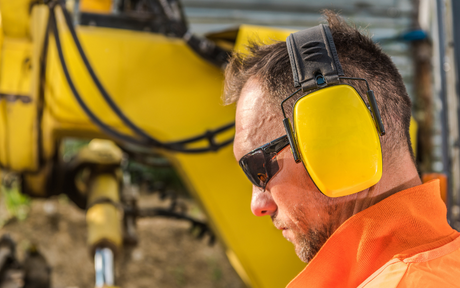 Worker at a construction site wearing yellow ear muffs and safety glasses.