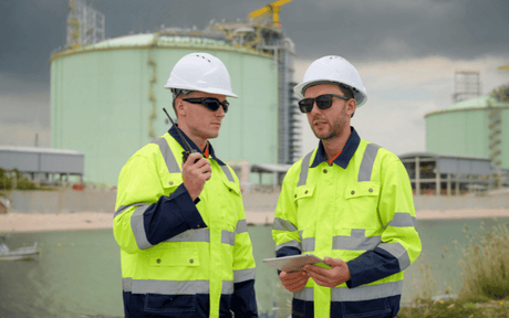 Two workers in high-visibility clothing and hard hats standing in front of industrial tanks.