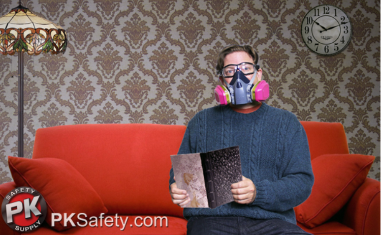 Man sits on red couch holding book and wearing a respirator.