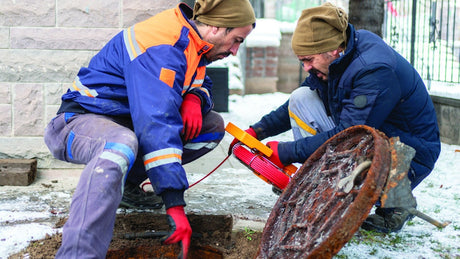 Workers working near manhole in the snow.