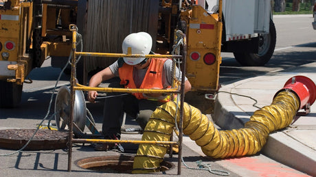 Worker using ventilation in manhole for confined space safety.