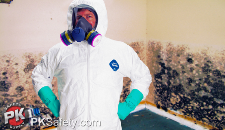 Man wearing white hazmat suit, respirator and gloves with black mold covering a wall behind him.
