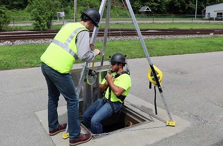 Worker helping another get into a confined space using a fall safety tripod.