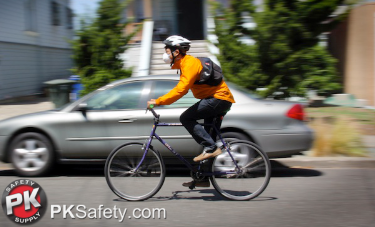 Person riding a bike while wearing a helmet and respirator.