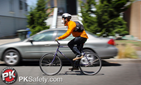 Person riding a bike while wearing a helmet and respirator.