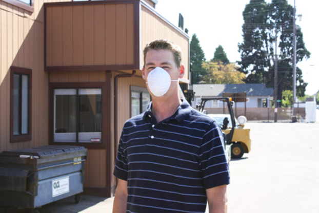 Man wearing dust mask respirator outside with building in background.