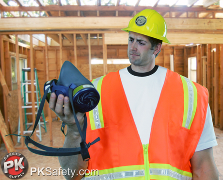 Construction worker looking at a respirator with home construction behind him.