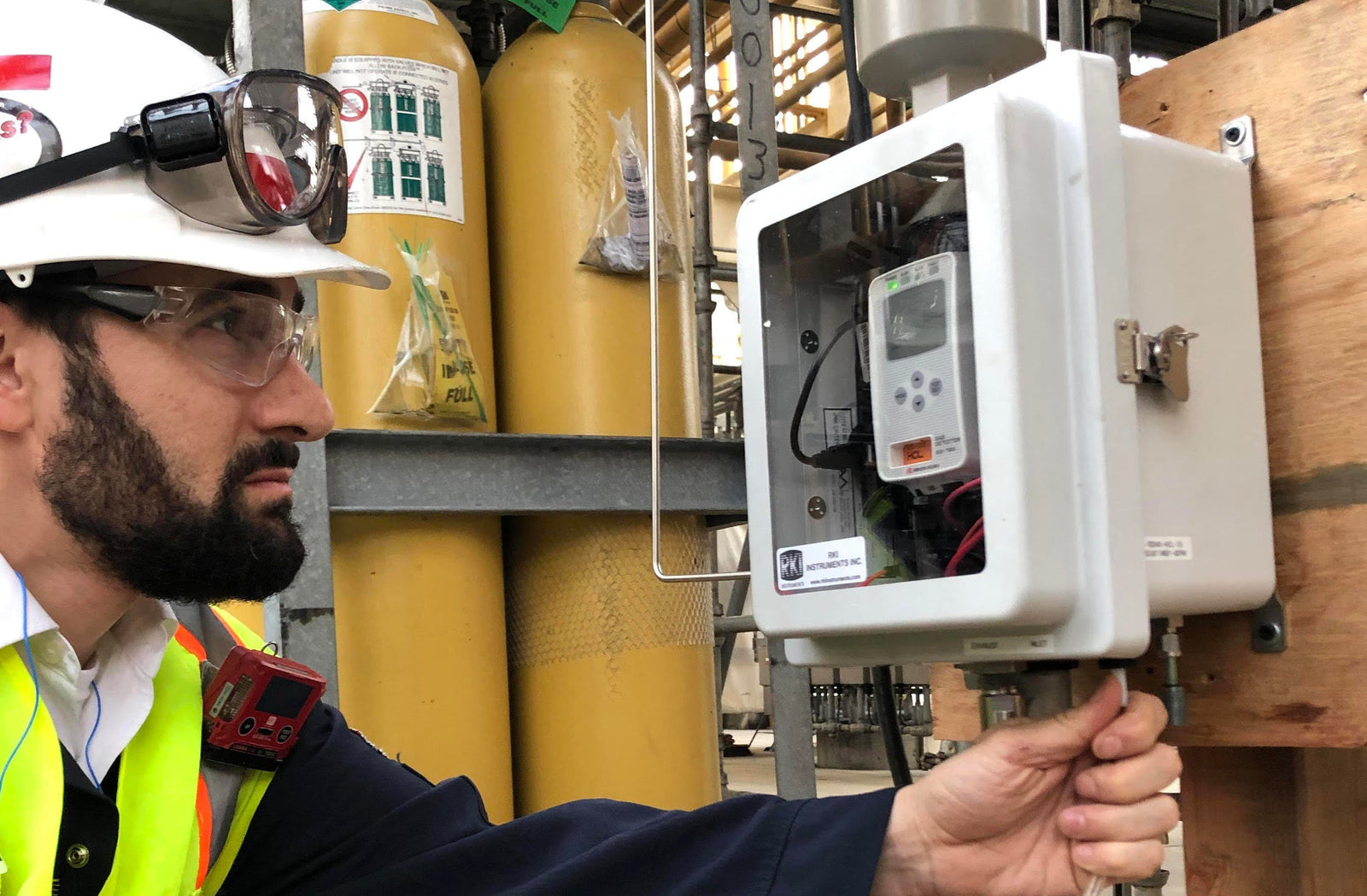A man with a hard hat and safety vest examines a meter, focused on his task in a construction environment.
