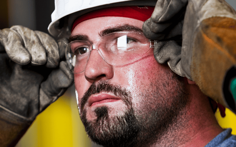 Closeup of worker holding his safety glasses, wearing gloves and hard hat.