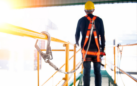Worker standing near railings wearing a harness and hard hat.
