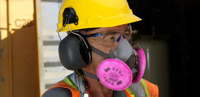 Construction worker wearing hard hat, ear muffs, glasses and half-face respirator.