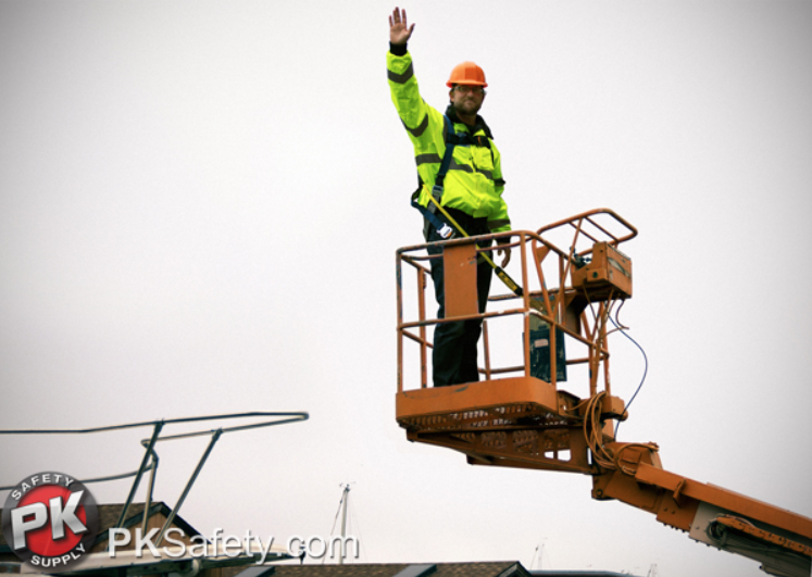 Man wearing hard hat and hi-vis jacket stands on lift waving.