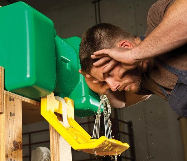 Man holding eyes open and leaning over eye wash station.