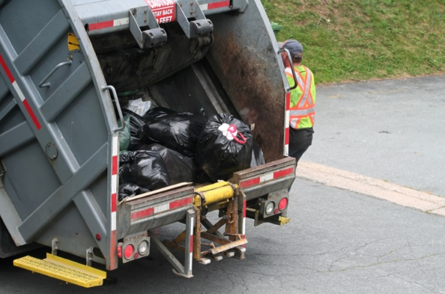 Garbage truck with plastic garbage bags and worker going to next stop.