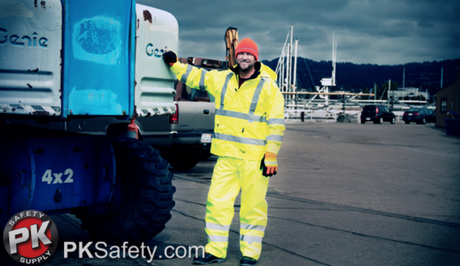 Man dressed in hi-vis workwear standing near vehicle at a marina with boats behind him.