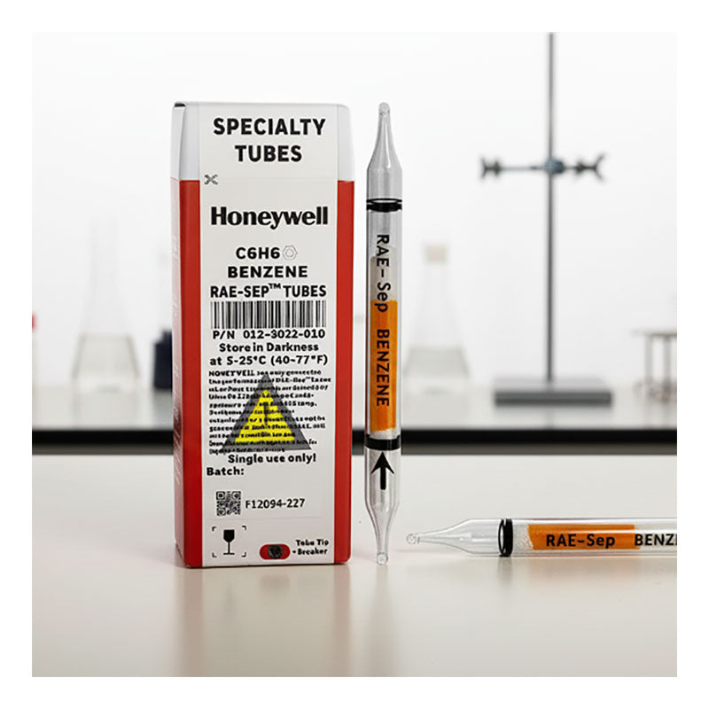 A box of RAE Systems Benzene Separation Tubes 012-3022-010 (10/Box) sits on a lab table beside a clear gas detection tube filled with orange liquid. Blurred lab glassware suggests compatibility with the UltraRAE 3000.