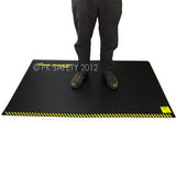 An individual stands on a Working Concepts ErgoKneel Extreme Standing Mat 5035, measuring 36 x 60 inches, featuring a black surface with yellow striped borders. Designed for support and comfort in extreme conditions, the mat is likely crafted from durable nitrile foam. The individual's face is not visible.