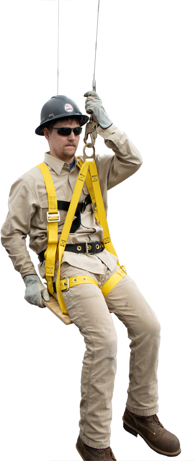 A person fully equipped with fall protection gear, including a helmet, gloves, and a high-visibility harness, demonstrates the French Creek Bosun Chair Work Seat 4754. They confidently sit on the platform outdoors with one leg bent, silhouetted by a fence and trees in the background.