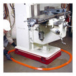 Wearing safety gear, an individual sets up an UltraTech Spill Berm Low-Profile Model 2052 by UltraTech International, an orange protective barrier, around a large industrial machine in the workshop. The machine is equipped with metal levers and is securely mounted on a red base to ensure efficient and safe operation.