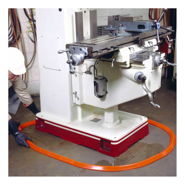 Wearing safety gear, an individual sets up an UltraTech Spill Berm Low-Profile Model 2052 by UltraTech International, an orange protective barrier, around a large industrial machine in the workshop. The machine is equipped with metal levers and is securely mounted on a red base to ensure efficient and safe operation.