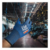 A gloved hand wearing a blue PIP G-Tek Paradox PolyKor A6 Foam Nitrile Glove 16-361 holds a small metal part in a factory setting, with machinery and equipment visible in the background.