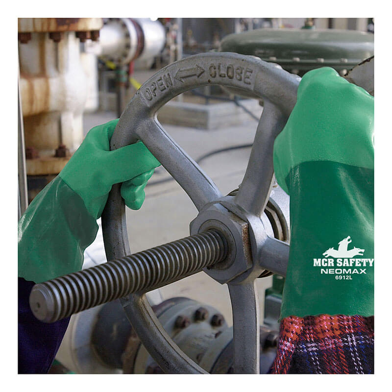 Someone wearing MCR Safety Neomax Neoprene Glove 6912 (12 pairs) is turning an industrial valve wheel marked "OPEN" and "CLOSE" in a factory or material handling setting.