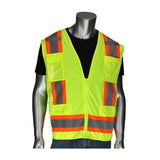 A mannequin is dressed in the PIP - Protective Industrial Products Two-Tone Surveyors Vest w/D-Ring, an ANSI Type R Class 2 vest in fluorescent yellow with orange and reflective gray stripes, layered over a black shirt and blue pants. This high-visibility garment includes multiple pockets and a zipper front, making it perfect for surveyors.