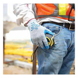 A construction worker wearing Showa Best SHOWA ATLAS 300 General Purpose Gloves, a safety vest, and jeans holds a tape measure by their side at a worksite with blurred equipment in the background.
