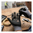 Wearing PIP MaxiFlex Endurance w/Full Nitrile MicroFoam Gloves 34-846, a person arranges screws, washers, and metal rods on their gloved hand, with assorted tools and hardware scattered on a workbench in the background.
