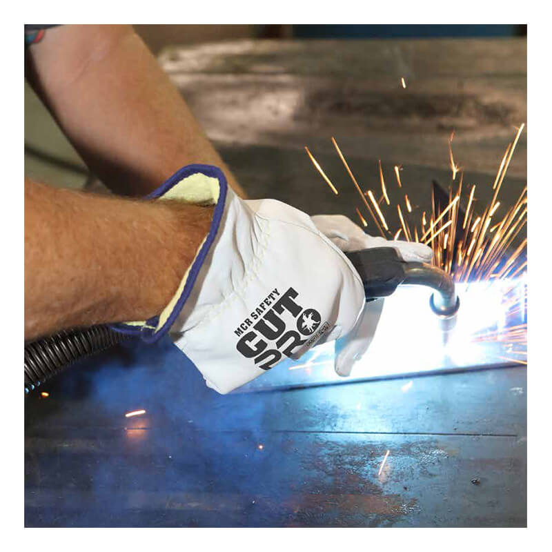 A person wearing protective gloves uses a welding tool on a metal surface, producing bright sparks. The glove reads “MCR Safety,” and features a DuPont Kevlar liner for enhanced protection, making the MCR Premium Grain Goatskin Driver Gloves 3601K (12 pairs) one of the leading cut resistant gloves available.