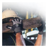 A construction worker wearing SHOWA 381 General Purpose Gloves by Showa Best and a hard hat carries a wooden beam on their shoulder, with a blurred industrial background.