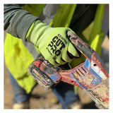 A person wears MCR Safety Cut Pro 18 Ga HyperMax Hi Vis Nitrile Micro Dotted Gloves (92748HV) while holding a dirty red power tool, paired with a yellow safety vest and long sleeves against a blurred outdoor background.