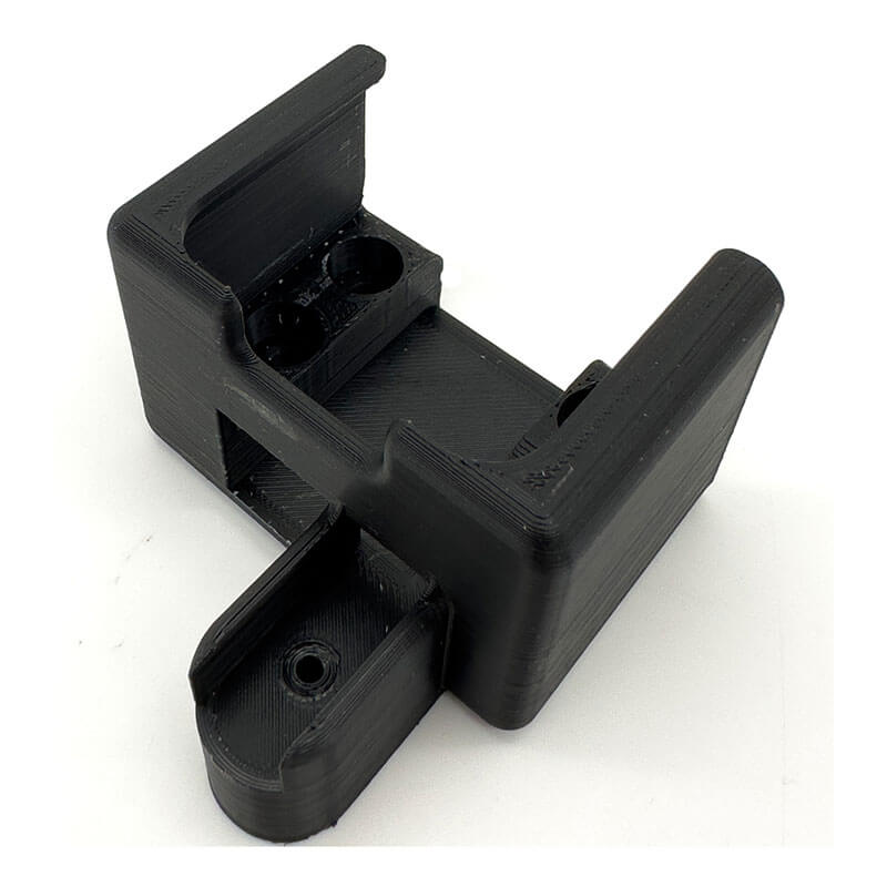 A black, 3D-printed plastic bracket with two slots and mounting holes, designed to secure the RKI Charging Cradle for GX-3R 49-2184 by RKI Instruments, photographed on a white background.