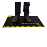 A person in brown work boots and blue jeans stands on a Working Concepts ErgoKneel Extreme Standing Mat 5032, featuring a black surface with yellow caution stripes. This anti-fatigue mat, made from closed cell foam pad material, provides comfort for long periods of standing while working.