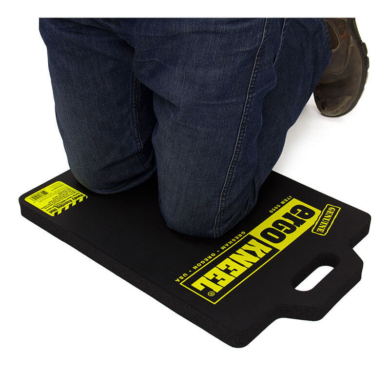 A person kneels on the Working Concepts Large ErgoKneel Kneeling Mat 5050 (14 x 21 in.), made of closed-cell foam rubber with yellow labeling and a built-in handle, providing comfort and protection during tasks.