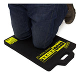 A person kneels on the Working Concepts Large ErgoKneel Kneeling Mat 5050 (14 x 21 in.), made of closed-cell foam rubber with yellow labeling and a built-in handle, providing comfort and protection during tasks.