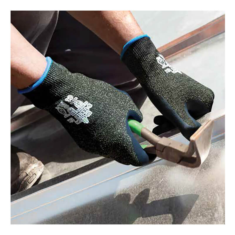 A person wearing SHOWA S-TEX 581 Cut Resistant Gloves by Showa Best, featuring a black design with a nitrile palm finish, uses a green-handled hammer on a surface, creating dust. Only the hands and part of the arms are visible.