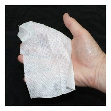 A hand gently holds a crumpled white disposable wipe, similar to the Coretex IvyX Pre-Contact Towelettes 300/Box 83644, against a dark background. The textured surface of the wipe provides skin coverage, enveloping the palm and part of the fingers in protection.