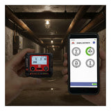 A person uses the RKI Instruments GX-3R Pro Gas Confined Space Monitor with Wireless Communication in one hand and checks gas readings on a smartphone, standing in a dim industrial tunnel with exposed pipes and ceiling lights.