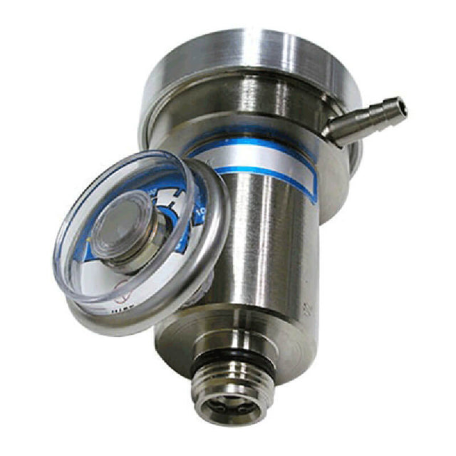 The RKI Calibration Gas Demand Flow Regulator by RKI Instruments includes a stainless steel pressure relief valve and circular gauge on top, utilizing demand flow regulator technology. This device features cylindrical components and fittings designed to regulate pressure in industrial settings, with a clear cap partially covering the gauge for precision control.
