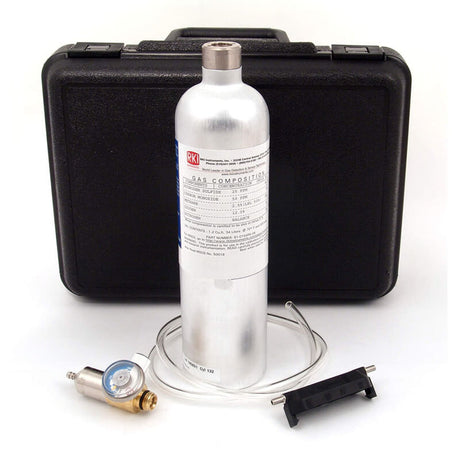 A silver gas cylinder labeled "Calibration Gas" is positioned in front of a black protective case, accompanied by a pressure regulator with gauge, clear tubing, and a black bracket. These components make up the RKI Instruments Manual Calibration Kit for GX-2009 Monitor from PK Safety Supply, an essential set for calibrating gas monitors.